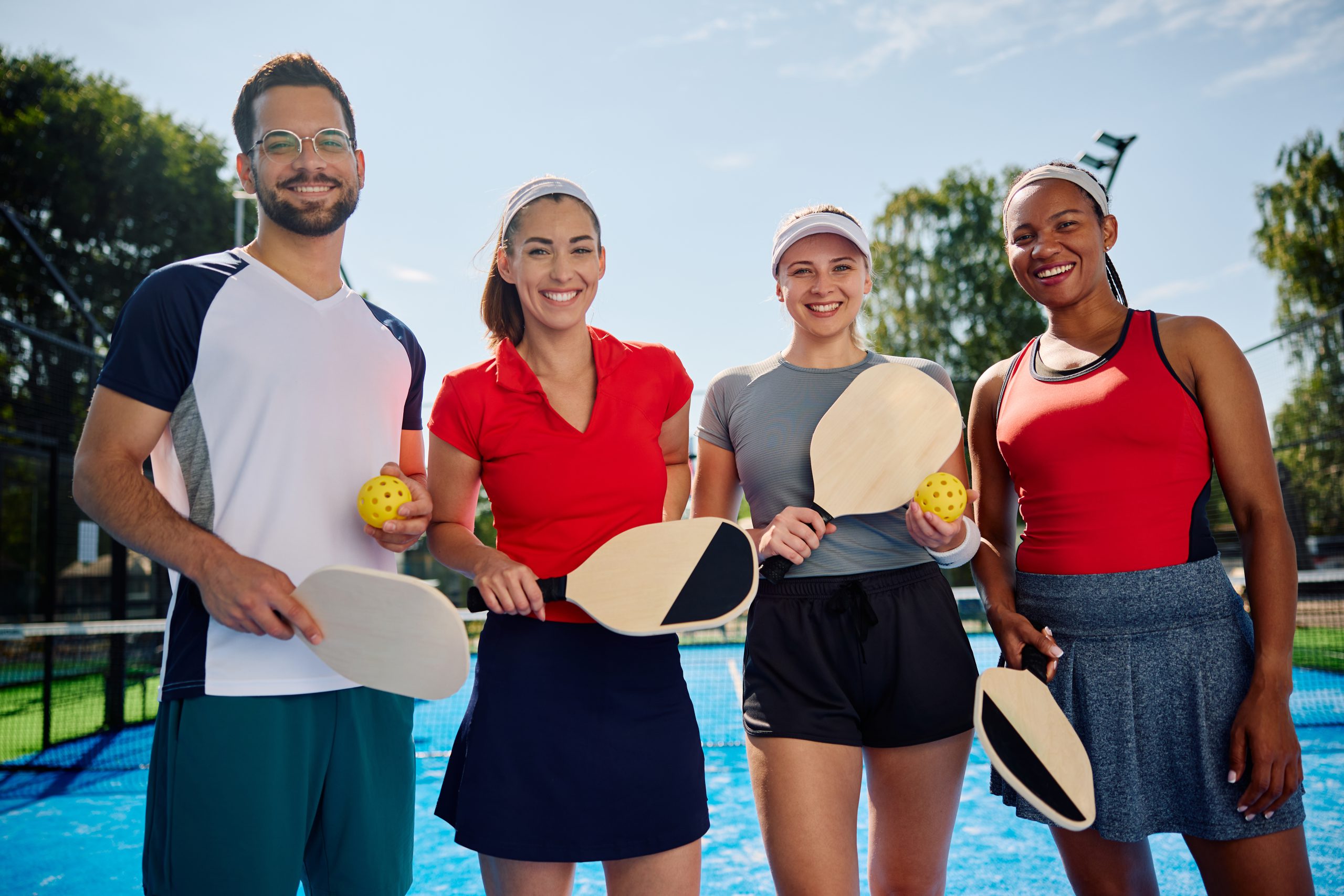 Multiracial group of happy friends playing pickleball and looking at camera.